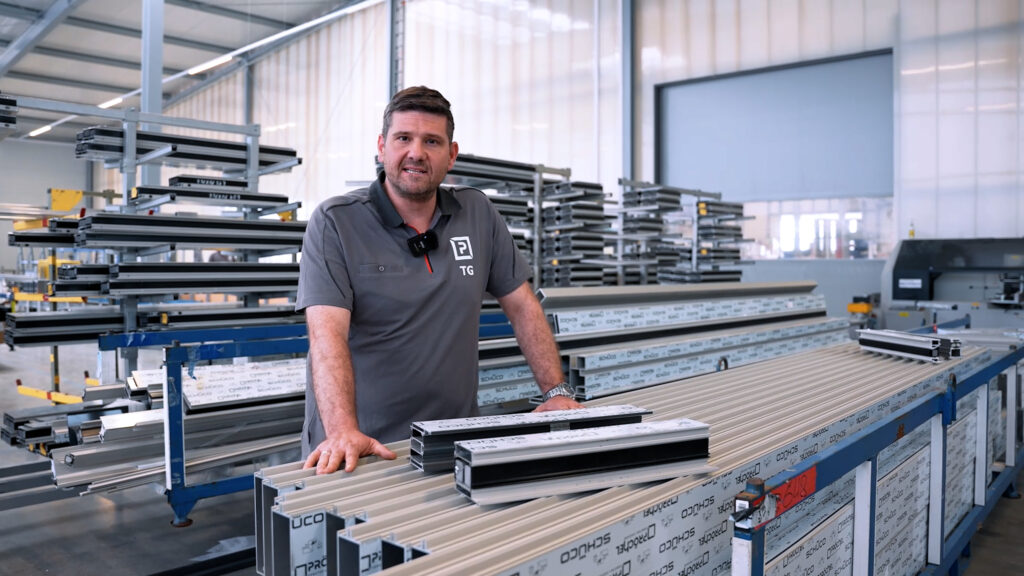 PRÖCHEL-Mitarbeiter steht vor einer Fläche mit diversen Aluminiumprofilen